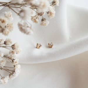 a pair of gold earrings on a white cloth with small flowers